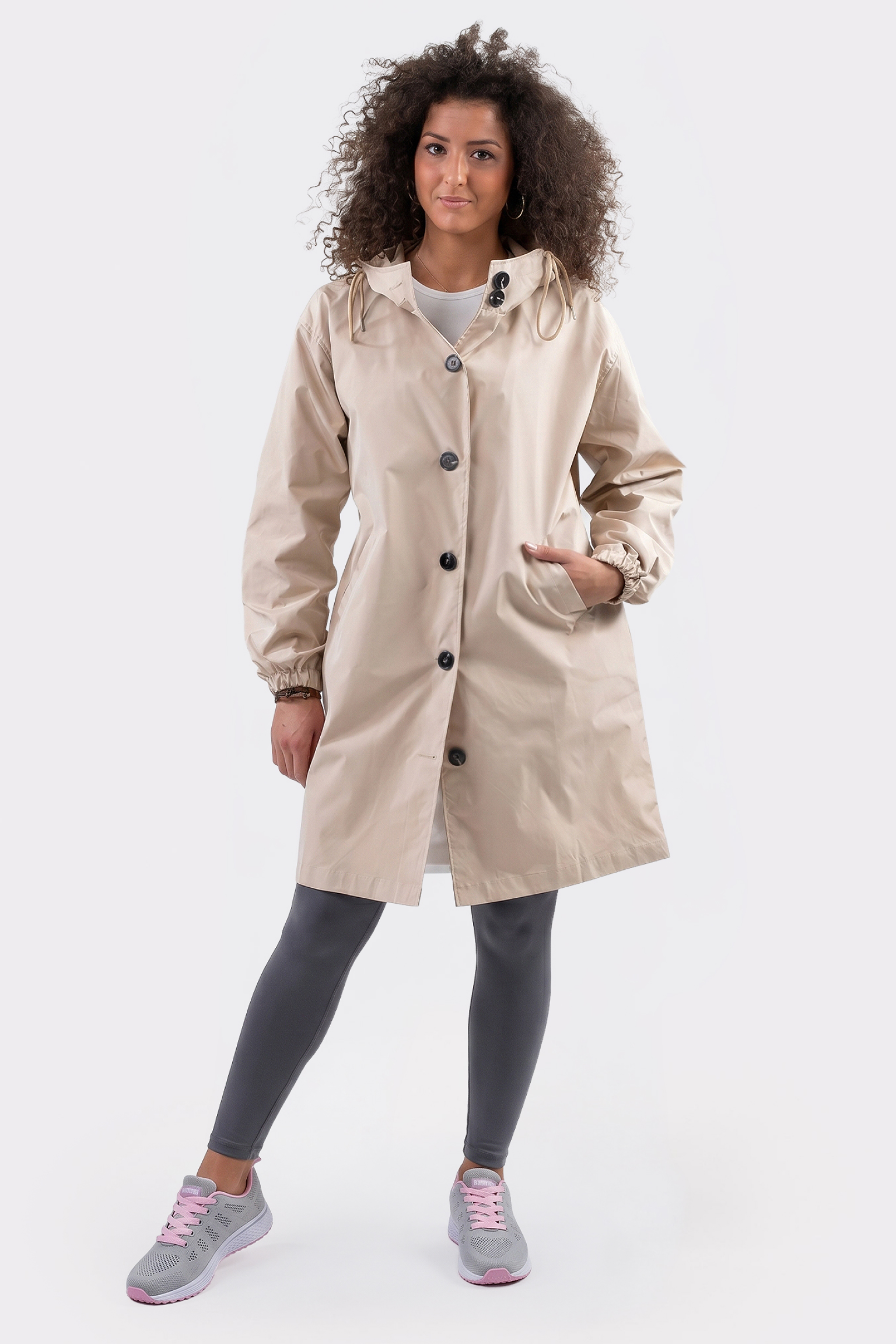 A person wearing the Icon Windbreaker Rain Jacket, gray leggings, and gray-pink sneakers stands against a plain white background with one hand in their pocket.