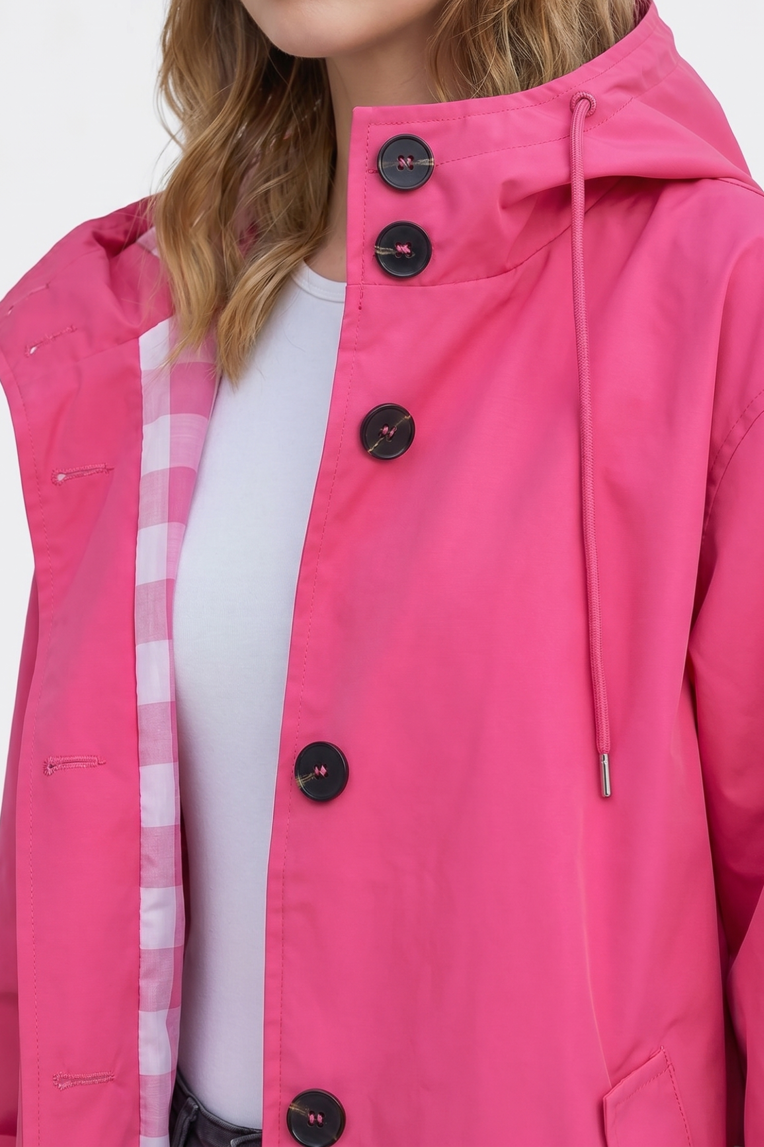 A person wears the Icon Windbreaker Rain Jacket in bright pink with black buttons over a white shirt. The jacket features a checkered pink and white lining visible near the collar. The person's face is partially out of frame.