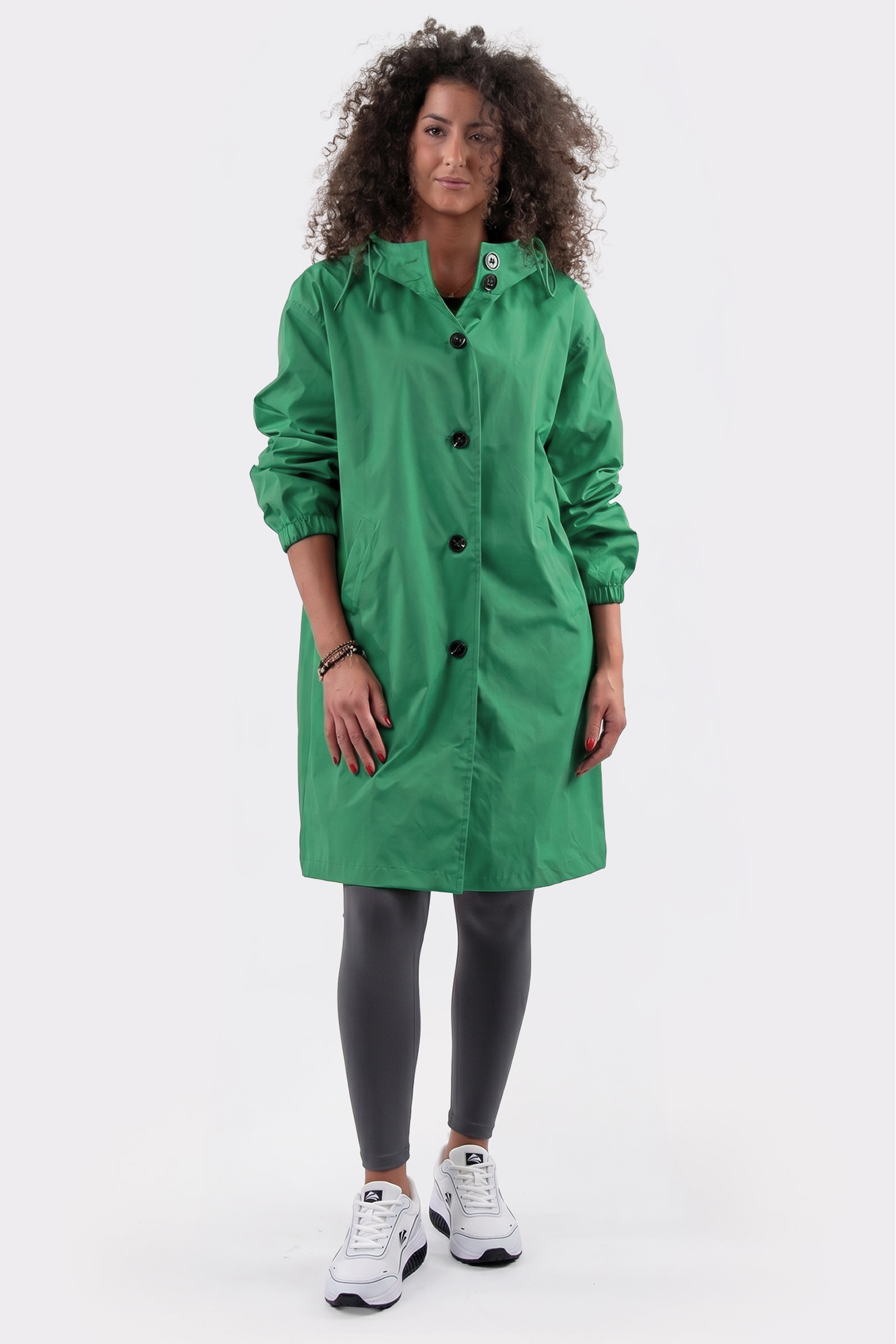 A person with curly hair is wearing the Icon Windbreaker Rain Jacket, dark leggings, and white sneakers, standing against a plain white background.