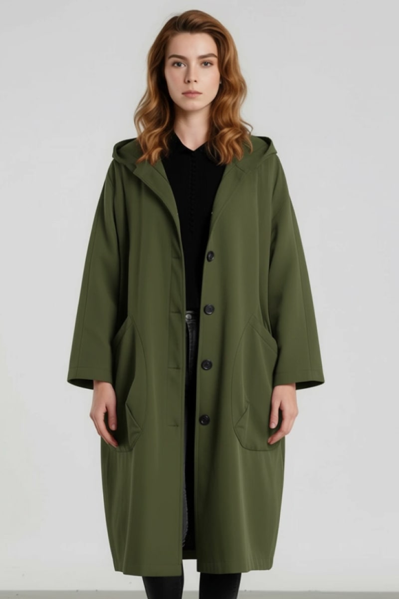 A woman with shoulder-length wavy hair stands against a plain background, wearing the looselyboho Army Green One Size Fits All Oversized Water Resistant Windbreaker Jacket over a black outfit, gazing straight at the camera.