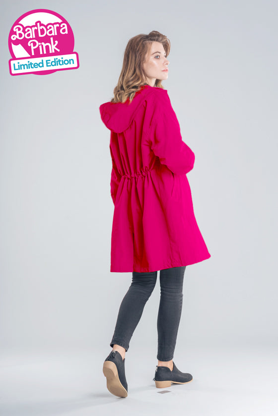 A woman stands facing away, showcasing the BARBARA PINK WINDBREAKER by looselyboho in a vibrant pink hue. Made from lightweight water-resistant fabric, this limited edition piece pairs effortlessly with her black pants and shoes. The text "BARBARA PINK WINDBREAKER Limited Edition" appears in the top left corner against a plain, light-colored background.