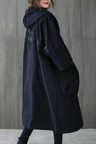 A person stands in front of a gray wooden wall wearing the Black One Size Fits All Oversized Water Resistant Windbreaker Jacket by looselyboho, complete with a hood for added mystery. Their partially visible face features striking red lipstick, enhancing the enigmatic vibe. The outfit is effortlessly chic, finished with black leggings and shoes.