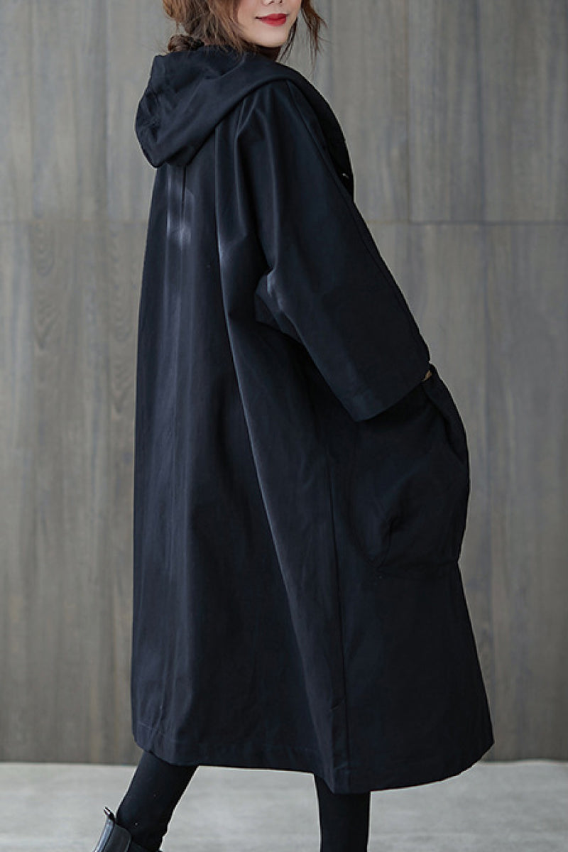 A person stands in front of a gray wooden wall wearing the Black One Size Fits All Oversized Water Resistant Windbreaker Jacket by looselyboho, complete with a hood for added mystery. Their partially visible face features striking red lipstick, enhancing the enigmatic vibe. The outfit is effortlessly chic, finished with black leggings and shoes.