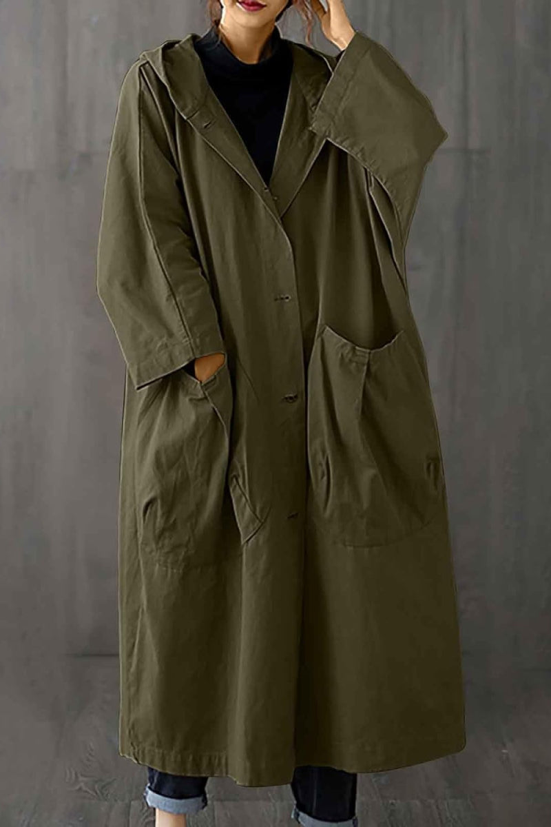 The individual is sporting the Army Green One Size Fits All Oversized Water Resistant Windbreaker Jacket by looselyboho. This chic olive green coat, featuring a hood and large pockets, is buttoned up as they stand against a plain backdrop, with their hands partially tucked into the pockets.