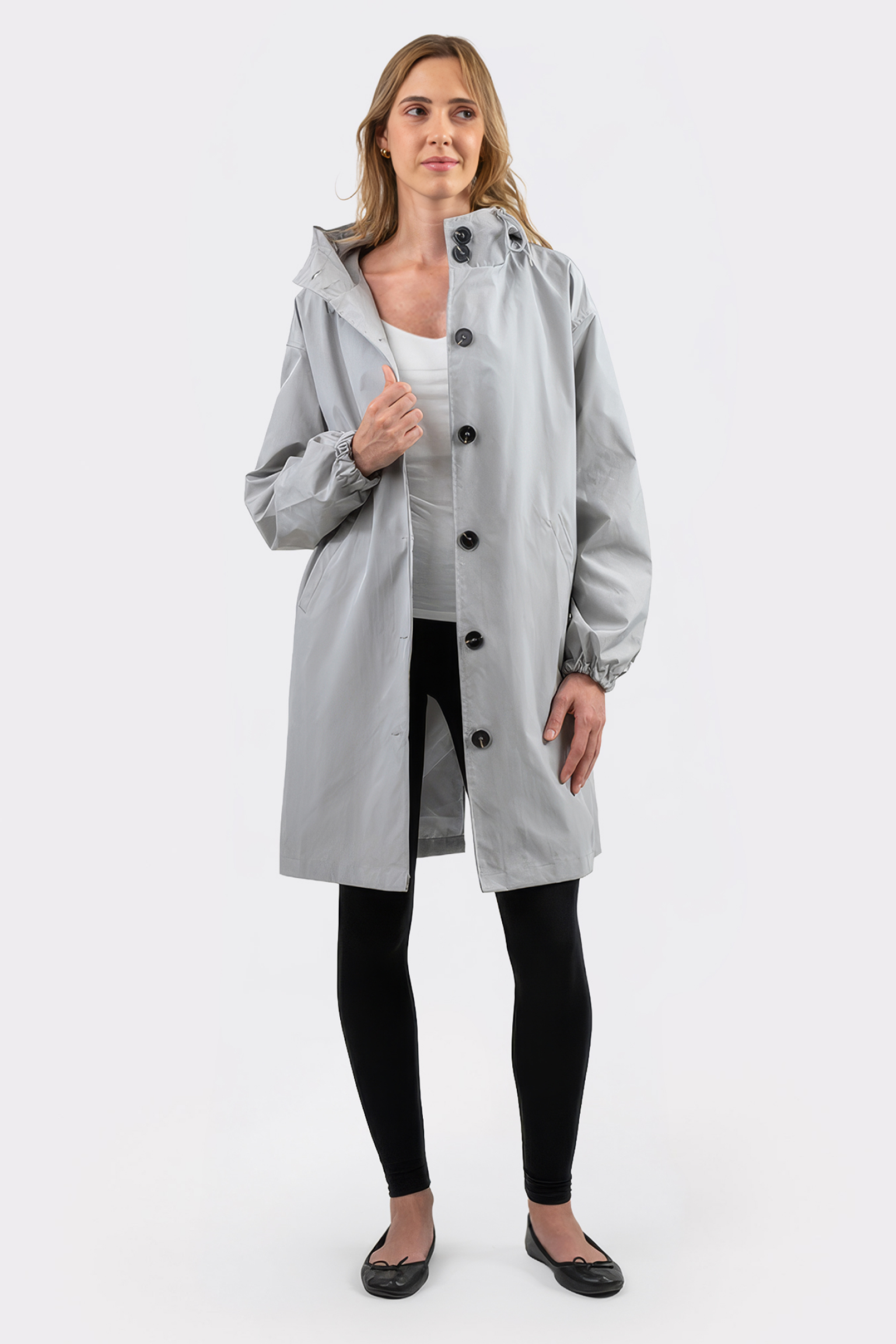 A woman stands facing forward in The Water Resistant Hooded Oversized Windbreaker Rain Jacket in light gray, paired with black leggings, a white top, and black flats against a plain white background.