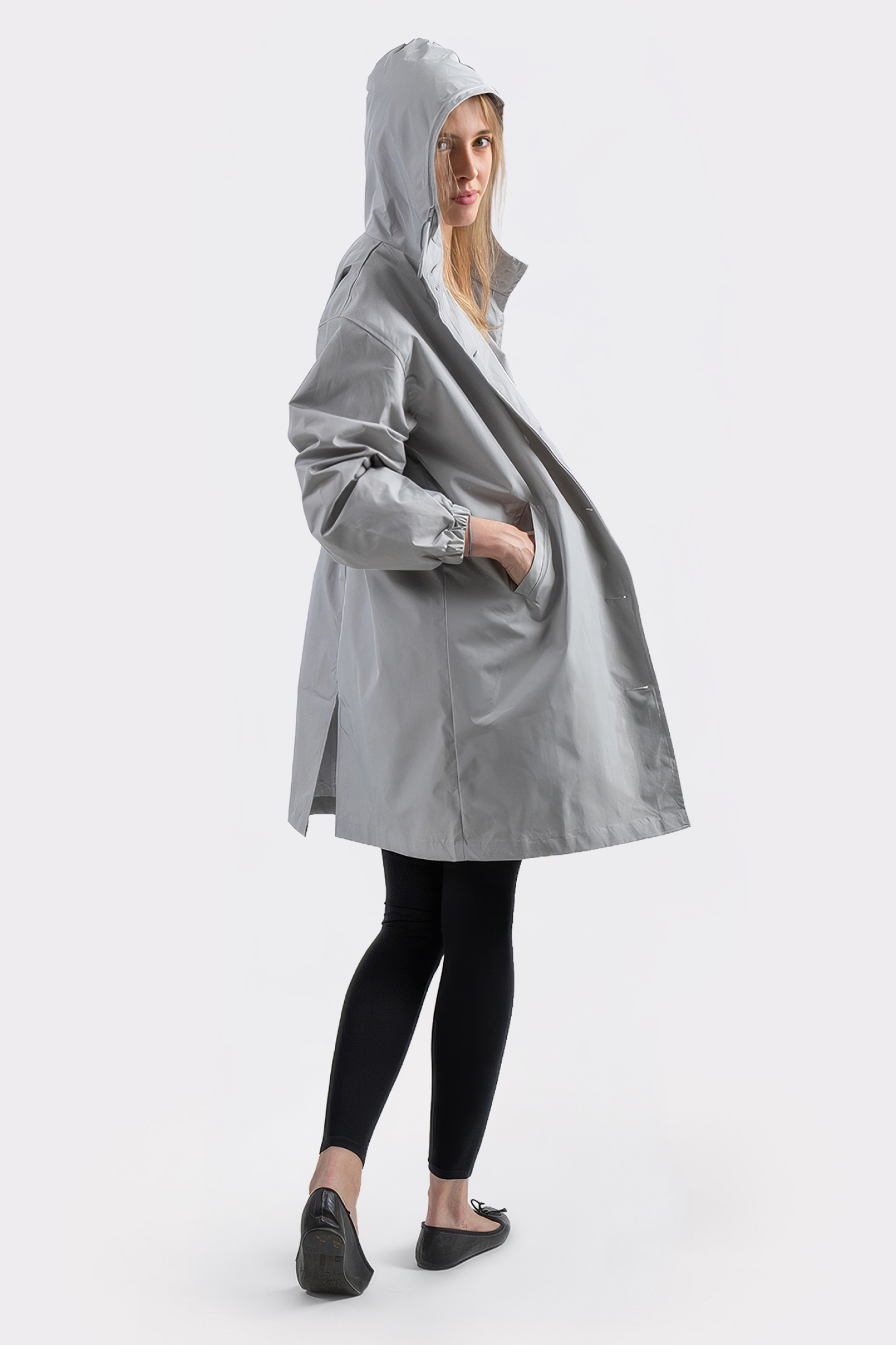 A person models The Water Resistant Hooded Oversized Windbreaker Rain Jacket in light gray, paired with black leggings and flats, standing against a plain white background with one hand in the jacket’s pocket.