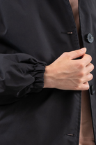 A person wearing the Icon Windbreaker Rain Jacket holds the front of the black long-sleeve jacket near the buttons with their right hand.