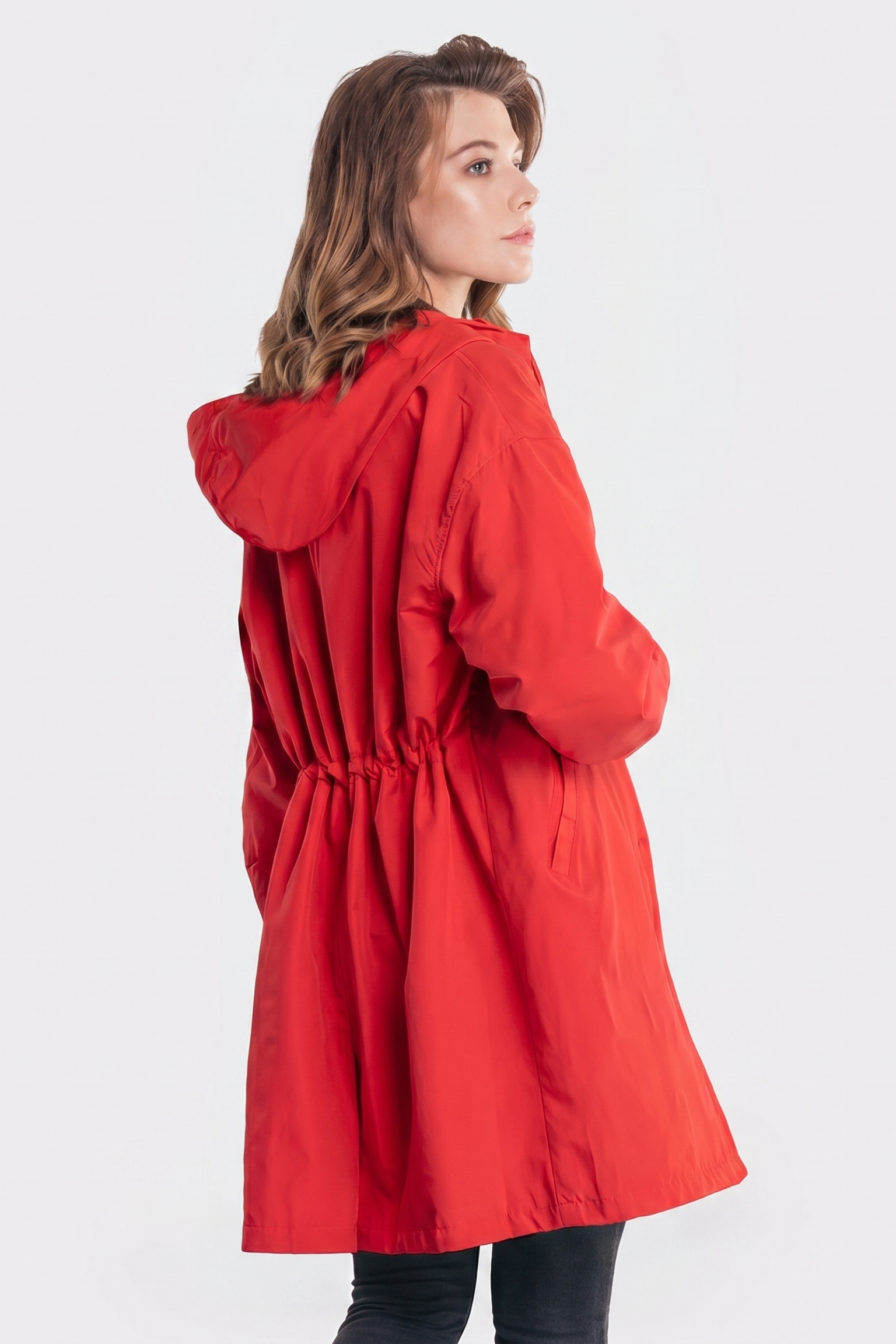 A person with light brown hair is seen from the back wearing The Water Resistant Hooded Oversized Windbreaker Rain Jacket in bright red, slightly turned to the side against a plain white background.
