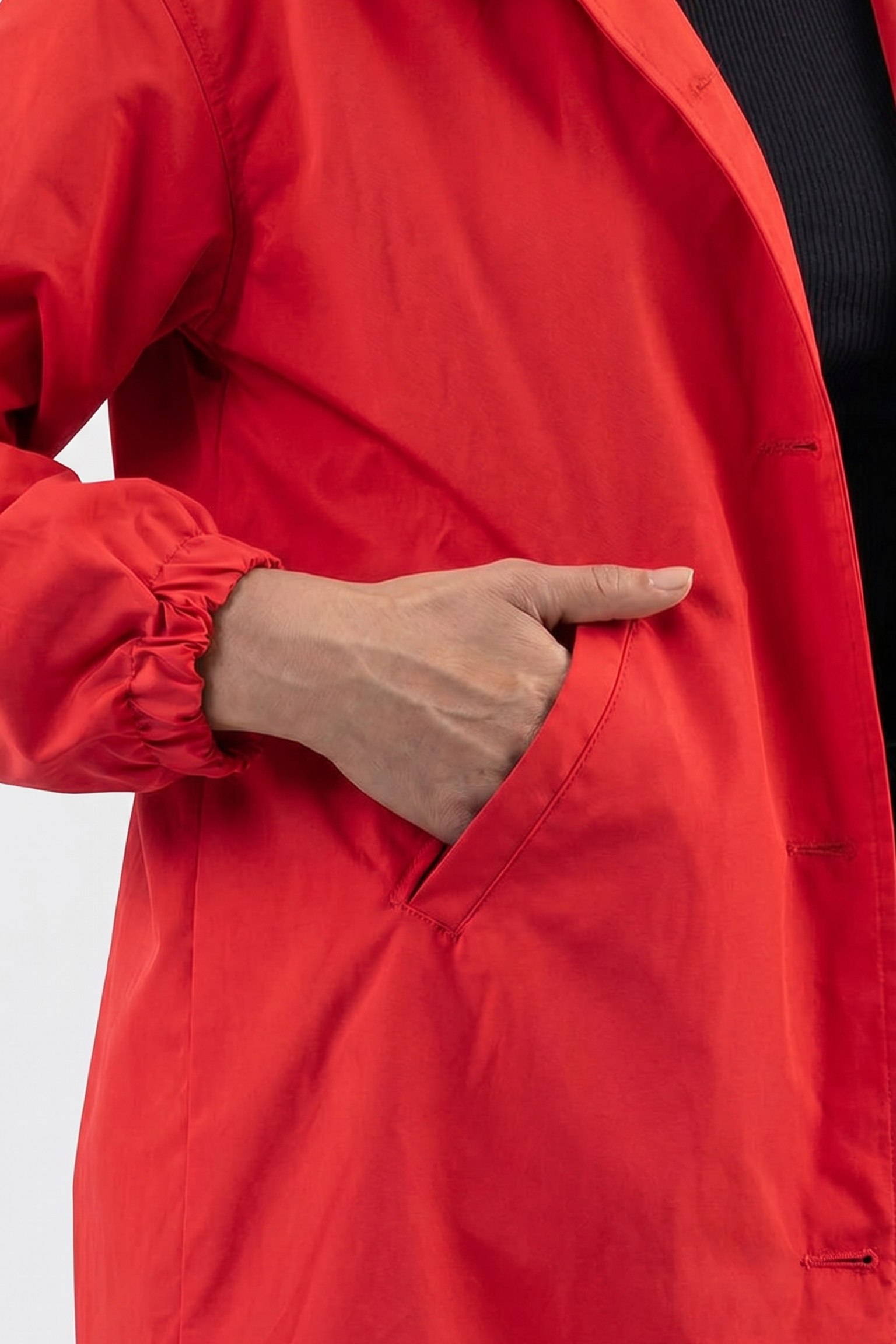 A person wears The Water Resistant Hooded Oversized Windbreaker Rain Jacket in bright red, with their left hand partly tucked into the pocket. The background is plain and light-colored.