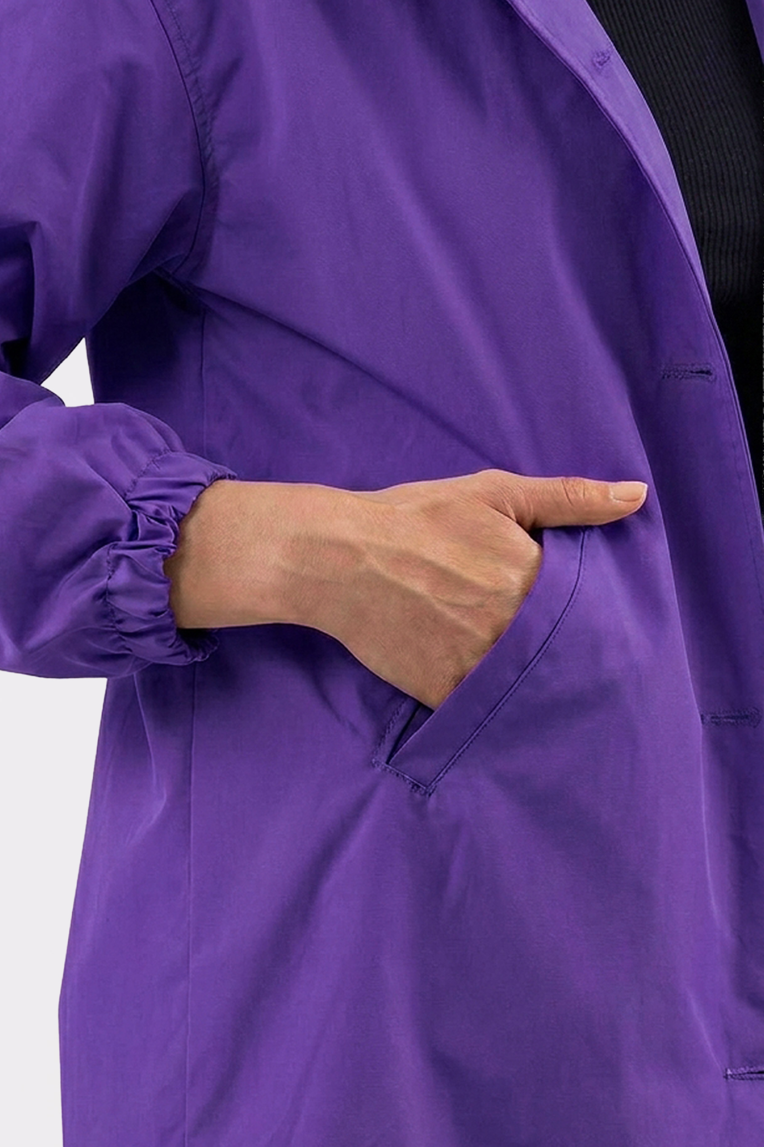 Someone wearing The Water Resistant Hooded Oversized Windbreaker Rain Jacket in purple with elastic cuffs has their right hand partially tucked into the jacket's side pocket.