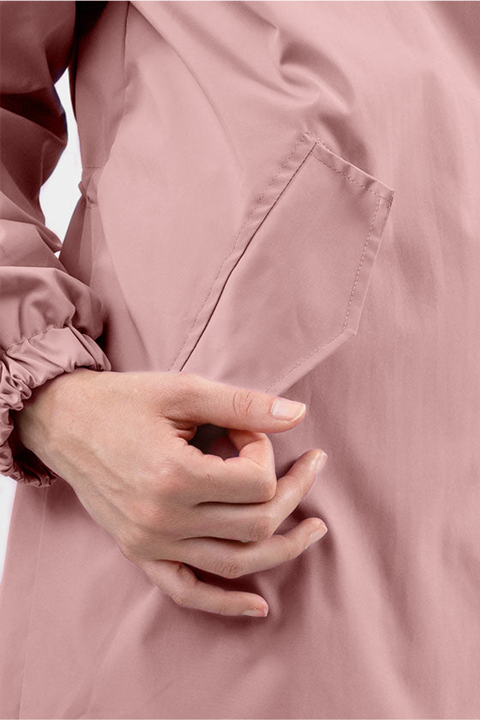 A person wearing the Water Resistant Hooded Oversized Windbreaker Rain Jacket in light pink with elastic cuffs puts their right hand into the jacket’s side pocket.
