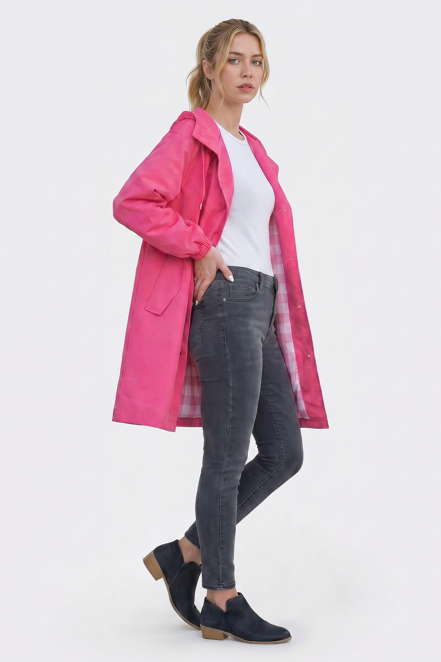 A woman with light hair pulled back and a neutral expression models The Water Resistant Hooded Oversized Windbreaker Rain Jacket in bright pink over a white tee, gray skinny jeans, and black ankle boots against a plain white background.