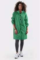 A person with curly hair is wearing the Icon Windbreaker Rain Jacket, dark leggings, and white sneakers, standing against a plain white background.
