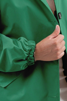 Someone gives a thumbs up while wearing the Icon Windbreaker Rain Jacket, identifiable by its green color and elastic cuffs. Only their hand, part of the arm, and the jacket are visible.