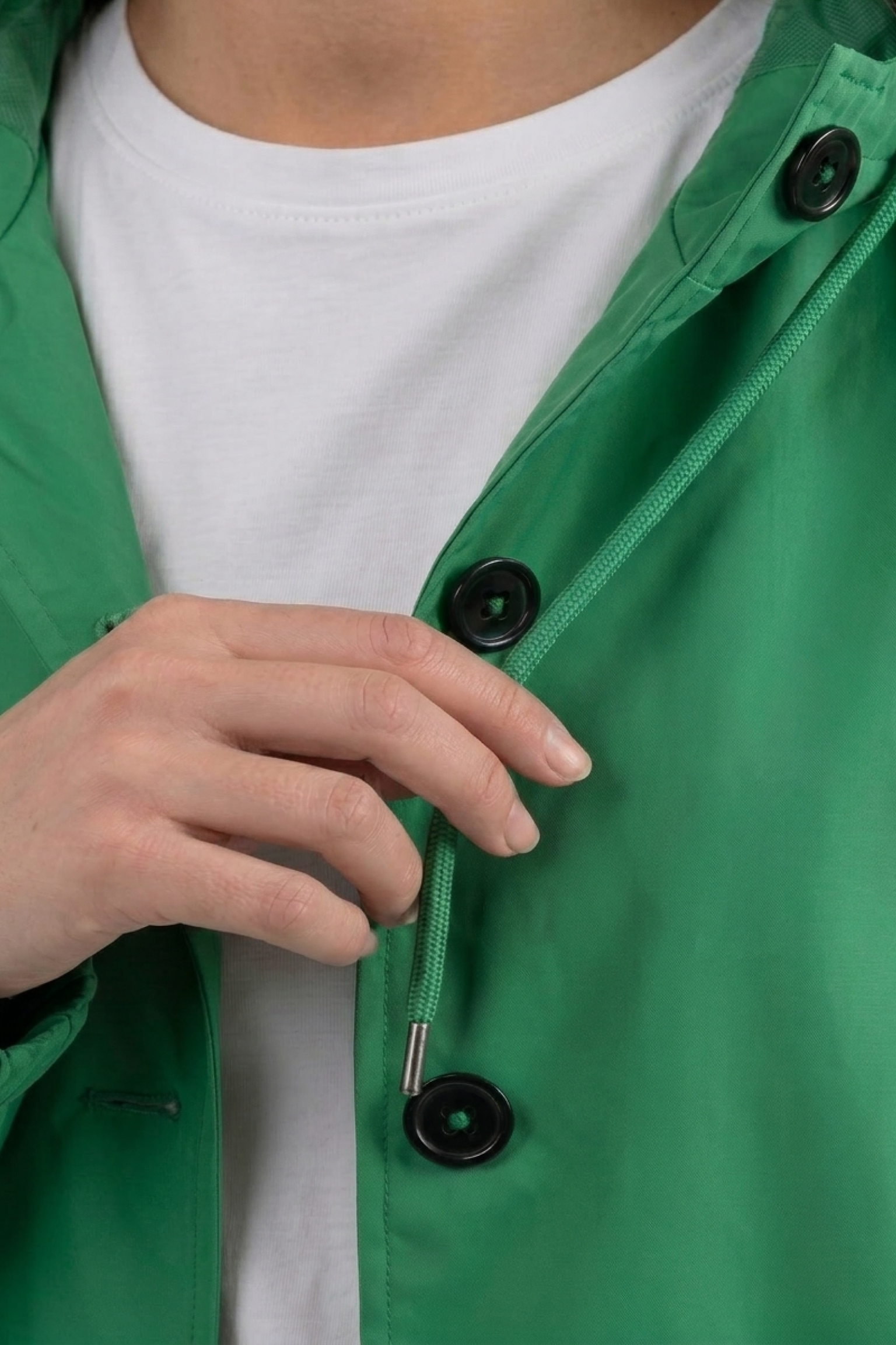 A person wearing a white shirt is shown fastening a black button near the chest on The Water Resistant Hooded Oversized Windbreaker Rain Jacket, with focus on the hand and green fabric.