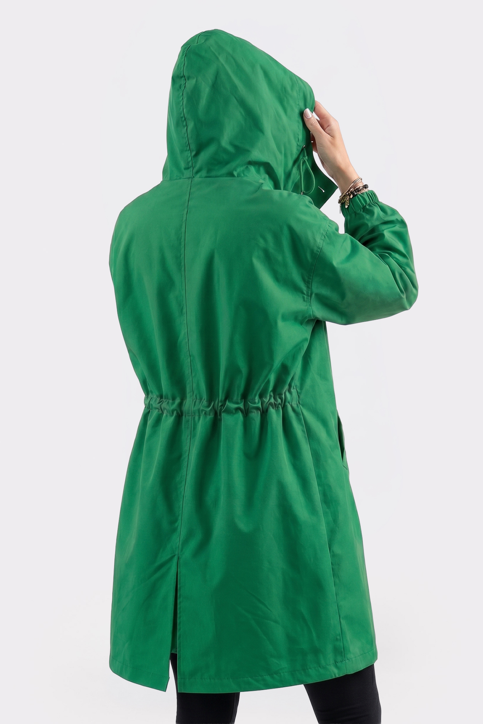 A person is seen from behind adjusting the hood of The Water Resistant Hooded Oversized Windbreaker Rain Jacket in bright green, featuring an elastic waistband and bottom slit, against a plain white background.