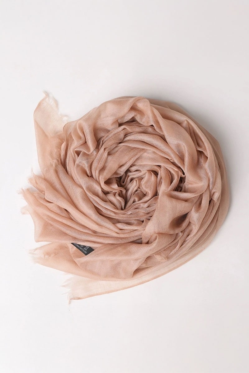 The Sandstone Dune 100% Cashmere Scarf by looselyboho, in light pink and semi-sheer, is displayed in soft folds on an off-white background. A small black tag detail adds a touch of elegance, perfect for refined winter layering.