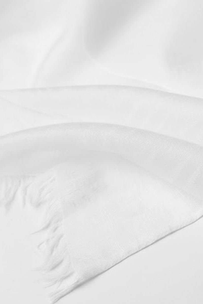 A close-up of the looselyboho Ivory Whisper 100% Cashmere Scarf, featuring a smooth, minimalist texture and soft fringed edges, elegantly laid flat with gentle folds to showcase luxurious simplicity.
