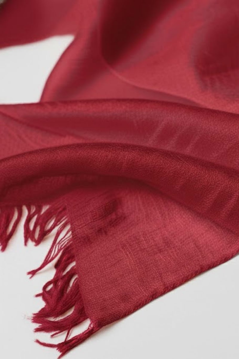 A close-up of the looselyboho Velvet Merlot 100% Cashmere Scarf, showcasing its soft texture and fringed edges, laid flat on a white surface.