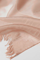 A close-up of the looselyboho Sandstone Dune 100% Cashmere Scarf in light pink shows its semi-sheer, fringed fabric with a smooth texture and wispy edges—perfect for elegant winter layering.