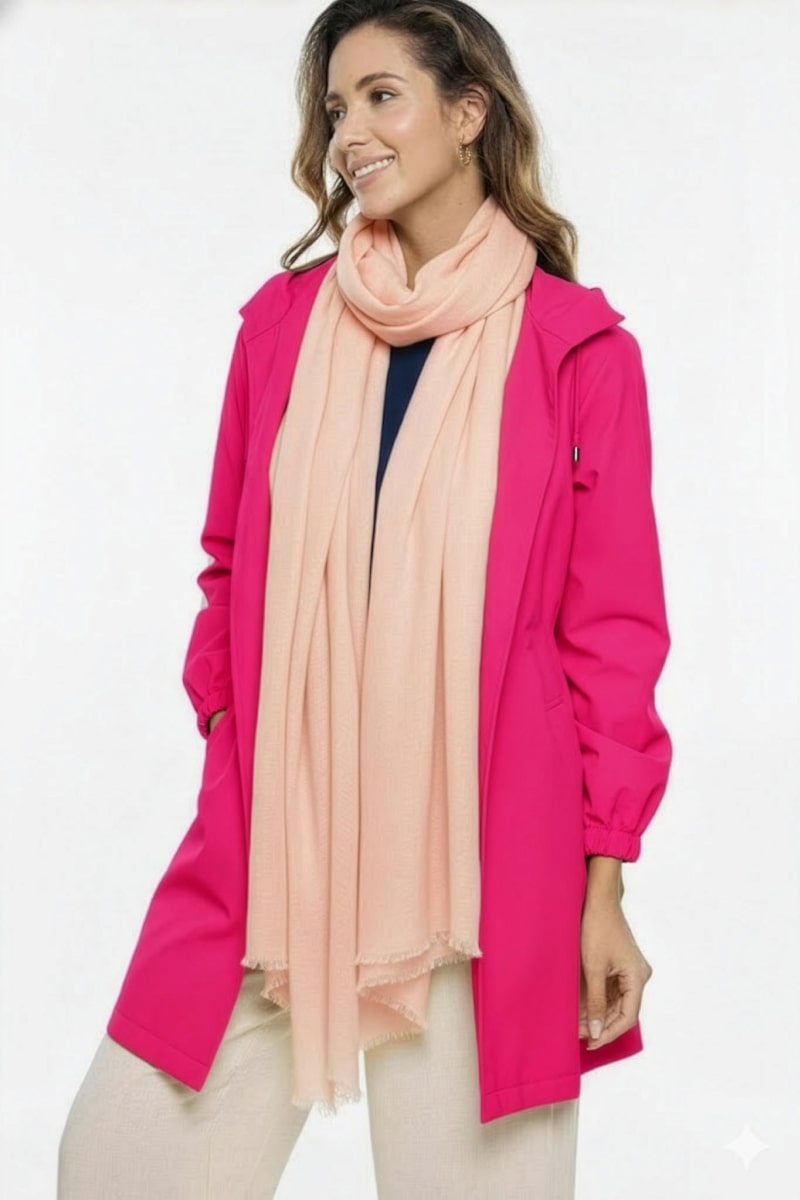 A woman stands against a white background in a bright pink coat, navy top, and beige pants, her outfit finished with the looselyboho Blush Rose 100% Cashmere Scarf—a luxurious winter accessory. Smiling, she gazes to the side.