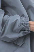 The image depicts a close-up of a person wearing The Windbreaker Jacket's POWDER BLUE WINDBREAKER. The focus is on the sleeve, which features an elastic cuff. With their arm slightly bent and part of their hand visible, the jacket exhibits a matte finish.