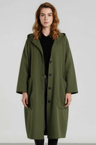 A woman with shoulder-length wavy hair stands against a plain background, wearing the looselyboho Army Green One Size Fits All Oversized Water Resistant Windbreaker Jacket over a black outfit, gazing straight at the camera.